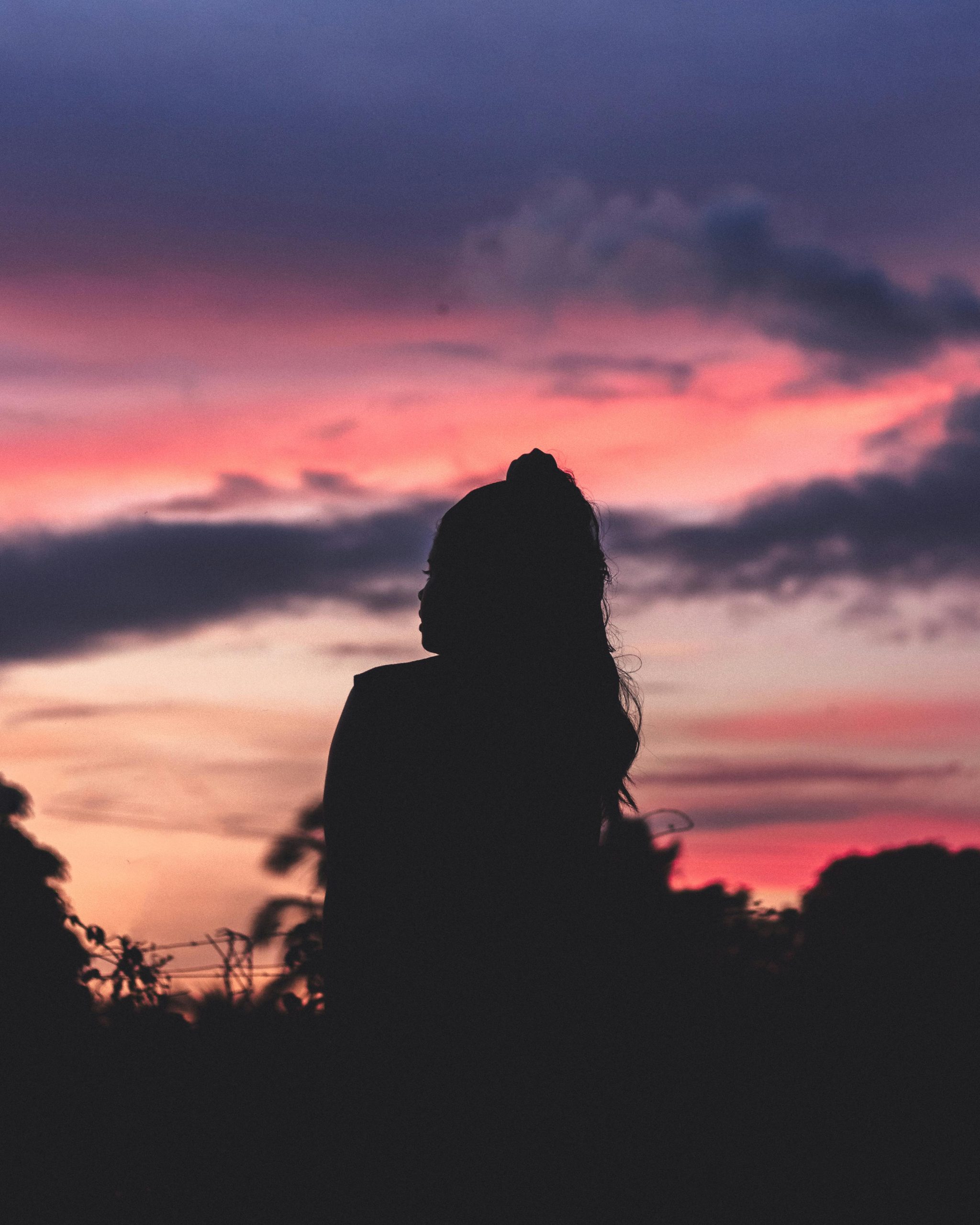 A woman silhouetted against a vivid sunset, blending in soft colors of dusk.