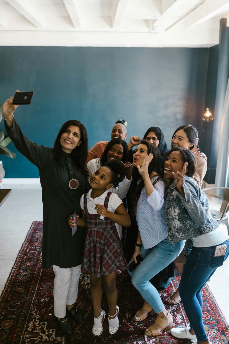 A diverse group of women and a girl joyfully capturing a selfie together in an indoor setting.